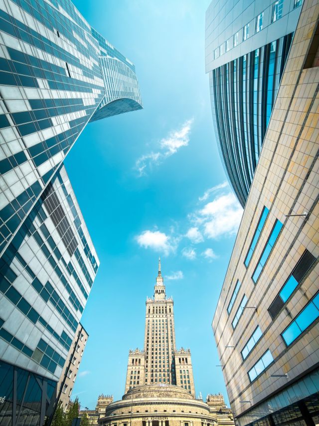 Pałac Kultury i Nauki Warszawa między nowoczesnymi wieżowcami błękitne niebo